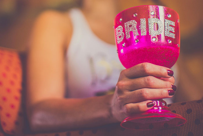 Bride holding a bright pink glittery glass with bride text, symbolizing obsession with control before the wedding.