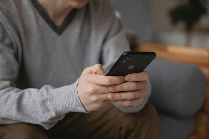 Person in gray sweater holding a phone, reflecting bride’s obsession with control affecting close friendships before wedding.