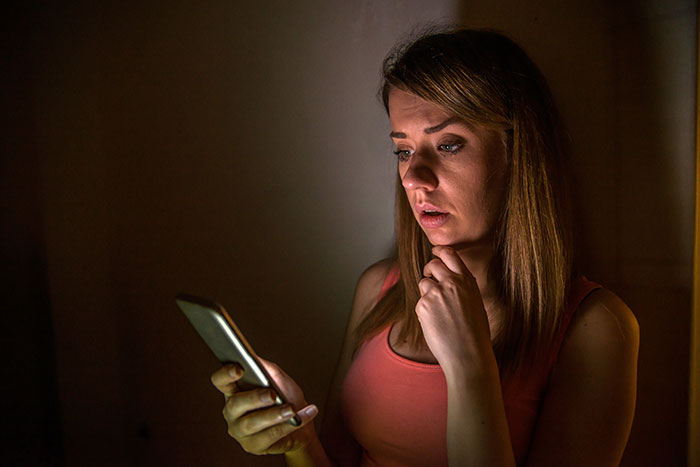Woman in dim light, using phone with a suspicious expression, trusting her gut instinct about a conspiracy.