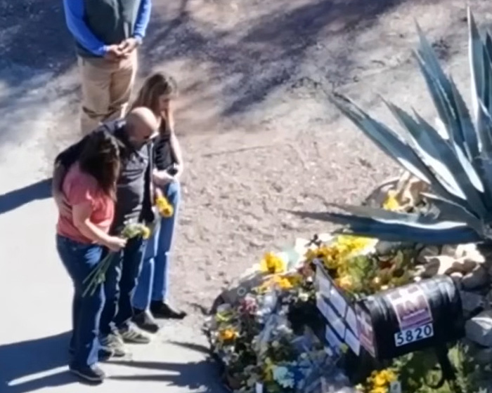 People gathered near a memorial site by Phoenix canal, holding flowers in the Nancy Guthrie case investigation.