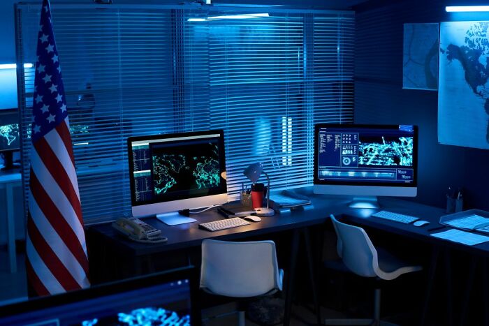 A dark control room with multiple monitors displaying maps and data, reflecting a mystery or unexplained phenomenon theme.
