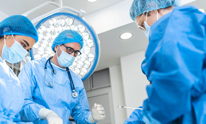 Surgical team wearing masks and scrubs performing an operation under bright hospital lights in a sterile environment