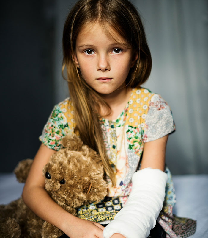 Young girl with a cast on her arm holding a teddy bear, reflecting hospital experiences so horrible they linger in memory.