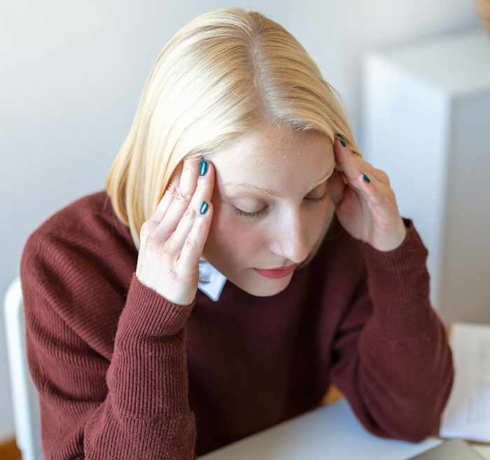 Woman in a brown sweater holding her head, portraying stress related to hospital experiences and healthcare frustrations.