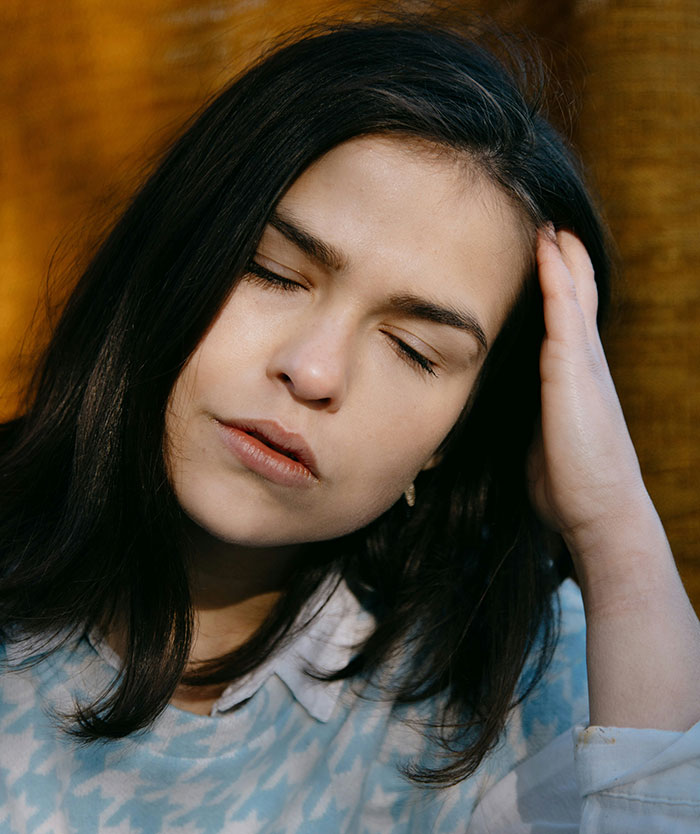 Young woman with eyes closed holding her head, showing signs of pain and distress related to hospital experiences.