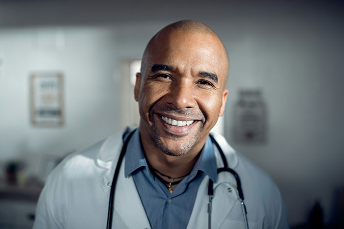 Smiling doctor wearing a white coat and stethoscope in a hospital setting related to hospital experiences.