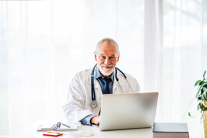 Senior male doctor with stethoscope using laptop, representing hospital experiences and medical care concerns.