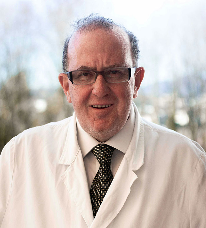 Middle-aged man in a white coat and glasses, smiling, representing hospital experiences and healthcare services.