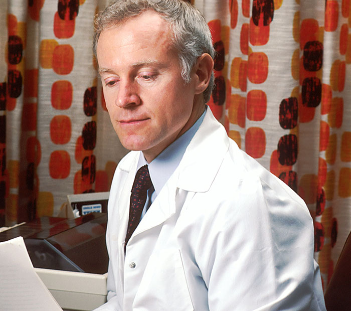 Male doctor in a white coat reviewing documents with a serious expression in a hospital setting.
