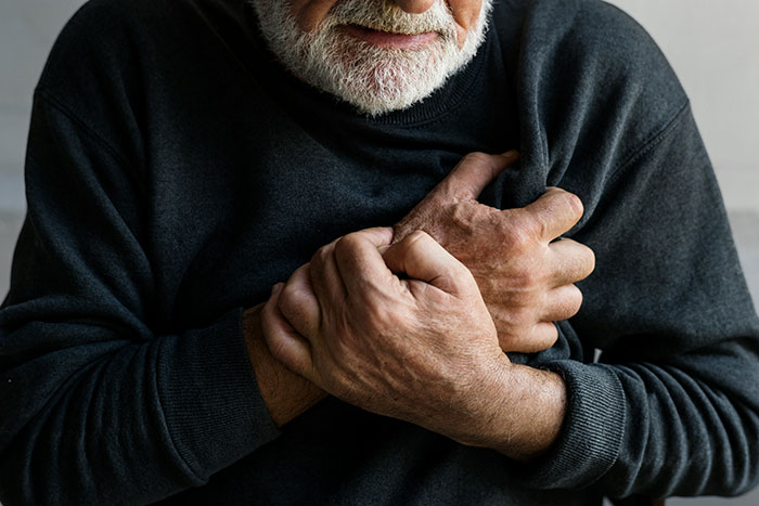 Elderly man in dark sweater clutching chest in pain, illustrating hospital experiences and health emergency concerns.