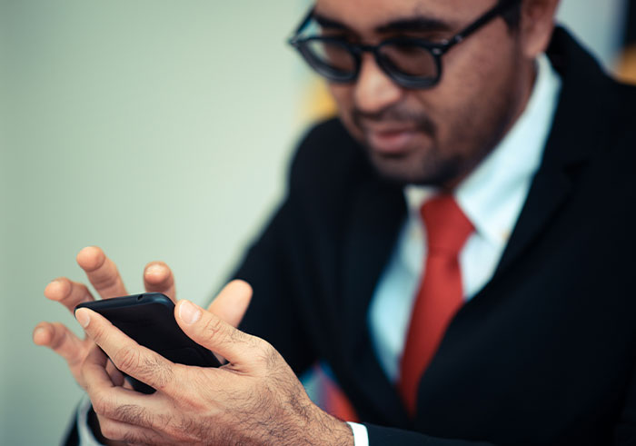 Man in black suit and red tie using smartphone, capturing one of the memorable funeral moments for all the wrong reasons