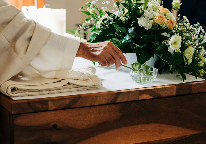 Person placing flower on wooden coffin decorated with a funeral floral arrangement during a memorable funeral moment