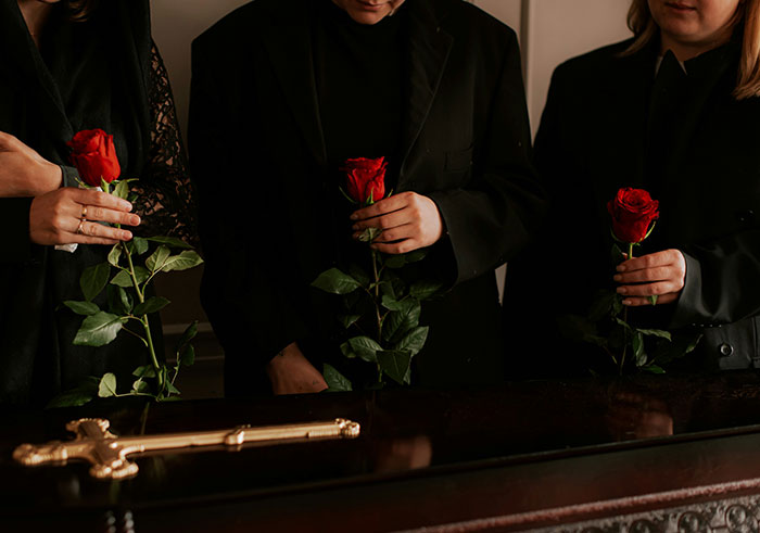 Three mourners dressed in black holding red roses during a funeral, reflecting memorable funeral moments.