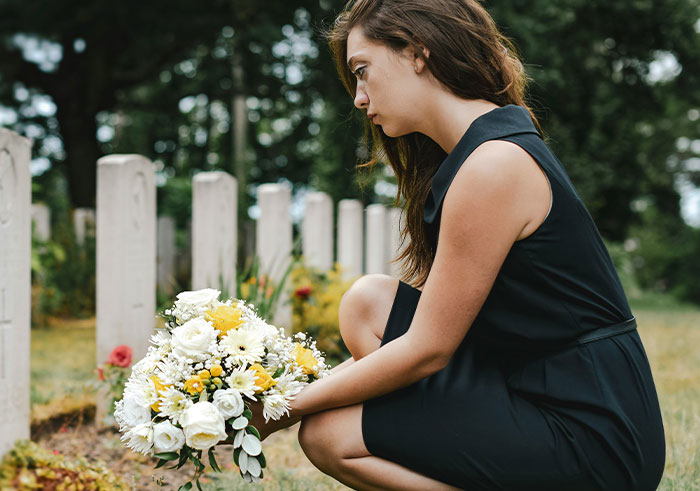 Young woman in black dress holding bouquet of flowers at a graveyard, reflecting on memorable funeral moments.