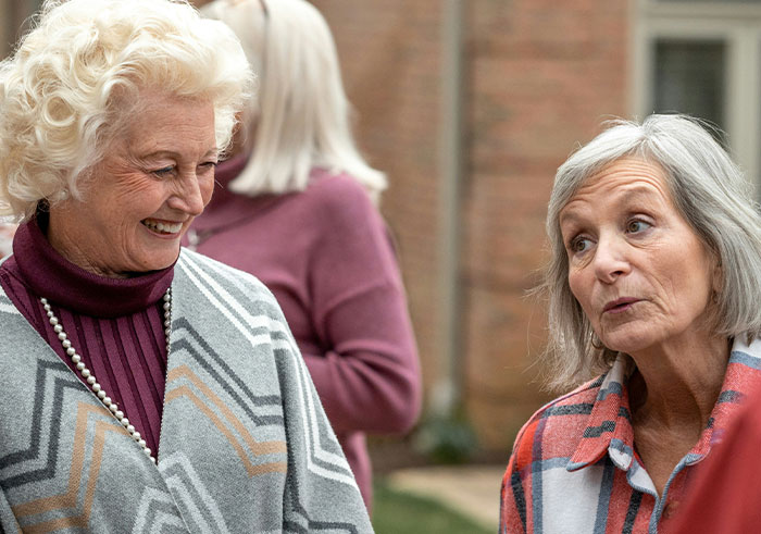 Two older women sharing a memorable conversation outdoors at a funeral, capturing unexpected moments.
