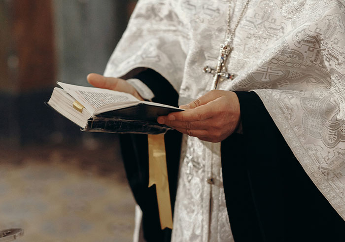 Clergyman wearing a white robe holding an open book, performing a memorable funeral moment ceremony.