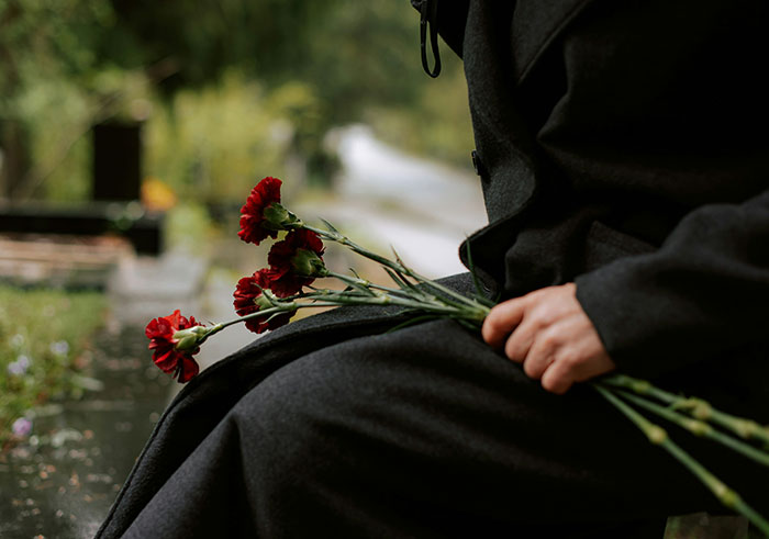 Person in dark clothing holding red carnations at a funeral, capturing memorable funeral moments for all the wrong reasons.