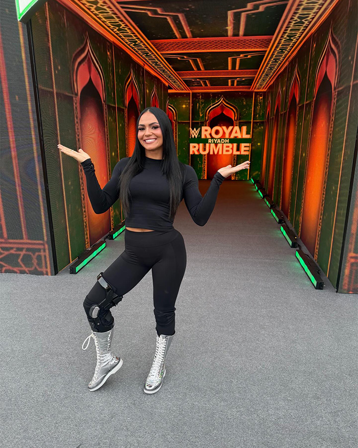 Pro wrestler Kiana James smiling at WWE Royal Rumble event, wearing black outfit and silver wrestling boots.