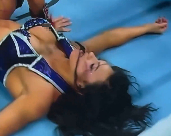 Pro wrestler Kiana James lying on wrestling mat during awkward wardrobe malfunction on live TV event.