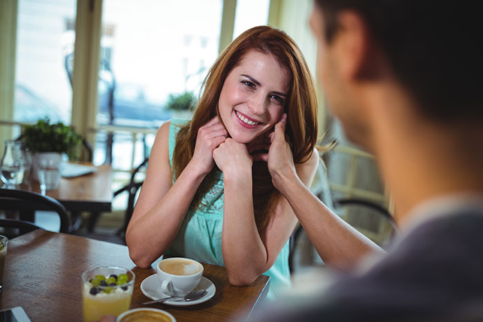 Young woman smiling warmly on a date with a single dad at a cozy cafe, enjoying coffee and conversation.