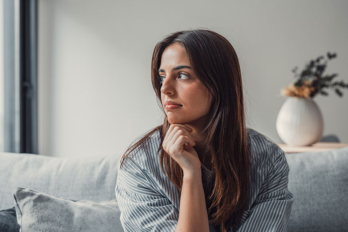 Young woman sitting on a couch looking thoughtful, representing emotions of dating a single dad in a modern home.