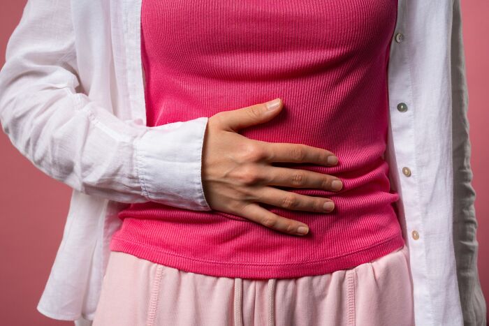 Person wearing a pink top and white shirt holding their stomach, illustrating interesting scientific facts to blow your mind today.