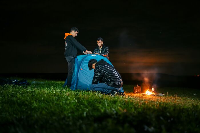 Three men setting up a tent near a campfire at night, capturing true scary camping and hiking stories.