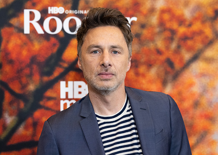 Zach Braff in a navy blazer and striped shirt attending an HBO event with autumn-colored background.