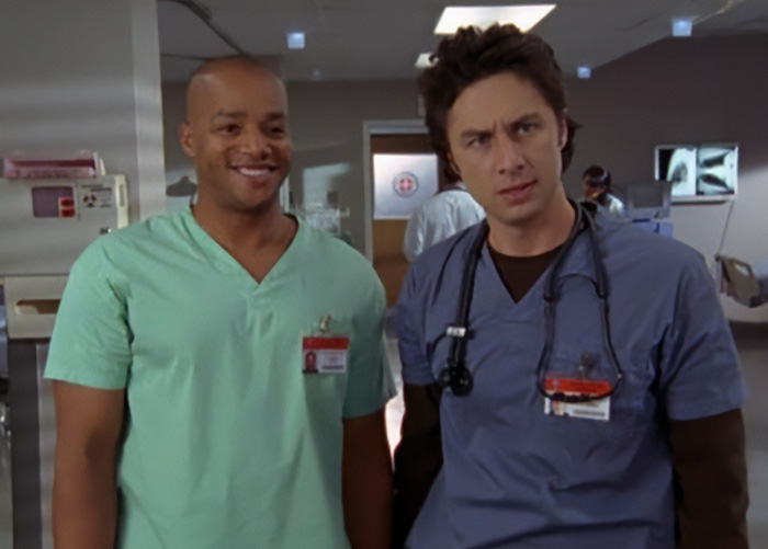 Zach Braff in hospital scrubs with co-star on set, reacting to bizarre accusation in a medical drama scene.