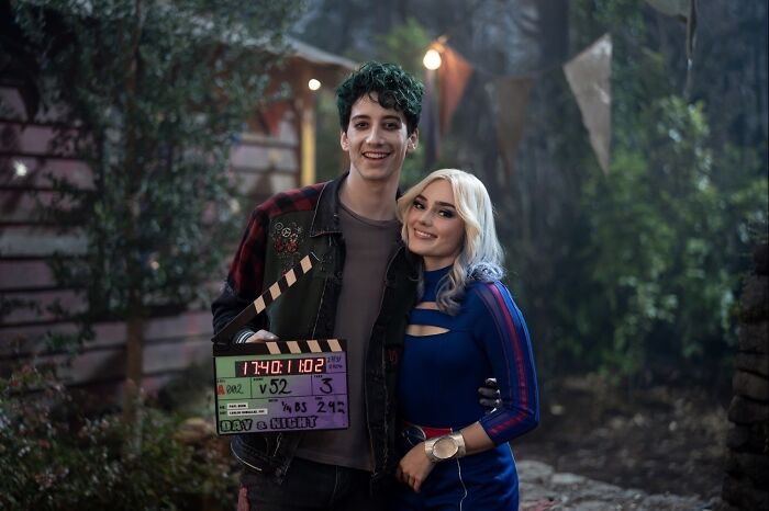 Two cast members smiling on set during Zombies 5 filming, holding a clapperboard in an outdoor night scene.