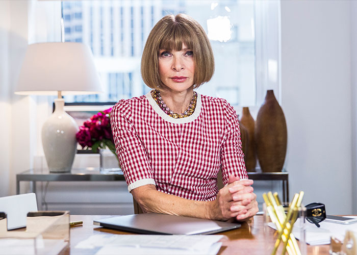 Anna Wintour sitting at a desk in an office, representing the reality of working for the Vogue icon.