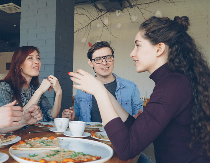 Young woman reacts with concern while sitting at a table with boyfriend and his close female friend and family. Young woman reacts with concern while sitting at a table with boyfriend and his close female friend and family.