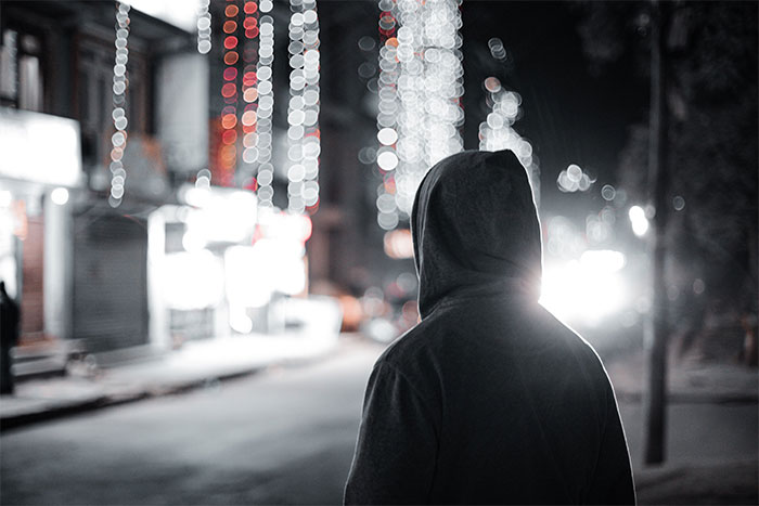 Man wearing dark hoodie at night on street with blurred lights, evoking a creepy confession and relationship doubt mood.