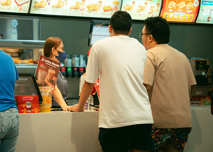 Entitled mom interacting with cashier at fast food counter as random guy waits to order food for her kids.