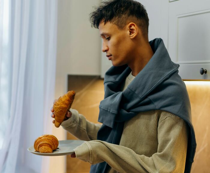 Young man holding a plate with croissants, illustrating moments of karma in everyday satisfying situations.