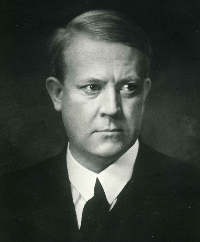 Black and white portrait of a serious man in a suit reflecting on massive betrayals in human history.