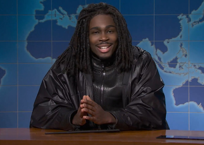 Actor portraying Black Snape in SNL skit discussing HBO Harry Potter reboot casting at a news desk with world map background.