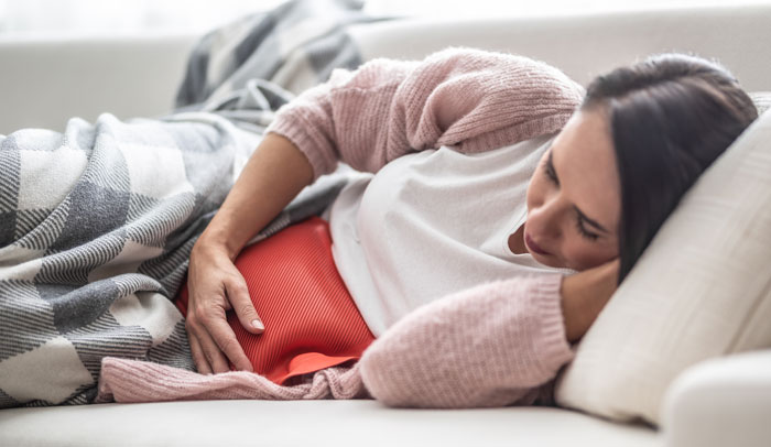 Woman lying on a couch, holding her stomach in discomfort, illustrating things women are tired of explaining to men.