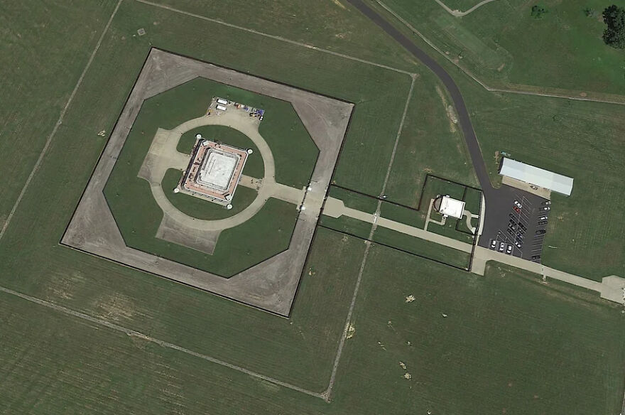An aerial view of a heavily secured, octagonal white building surrounded by green fields. The world's toughest security.