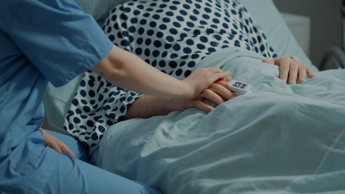 Healthcare worker holding the hand of a patient in bed, illustrating the emotional impact of oversleeping nightmares.