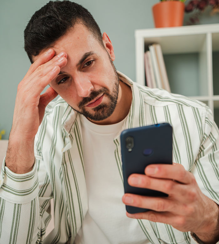 Man feeling stressed while looking at his phone, illustrating petty karma to bosses in workplace situations.