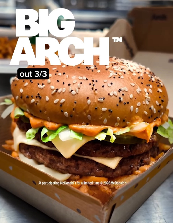 Close-up of McDonald&rsquo;s Big Arch burger with sesame bun, lettuce, cheese, and sauce in a cardboard box.