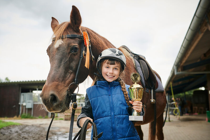 Young girl holding a trophy next to a horse, representing the golden child syndrome and the pressure of being perfect.
