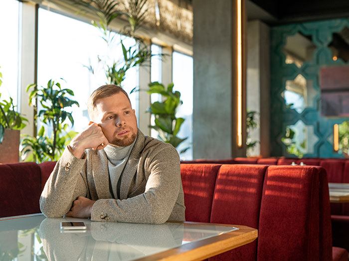 A man looking bored at a restaurant table, illustrating a horrible first date, with his phone beside him.