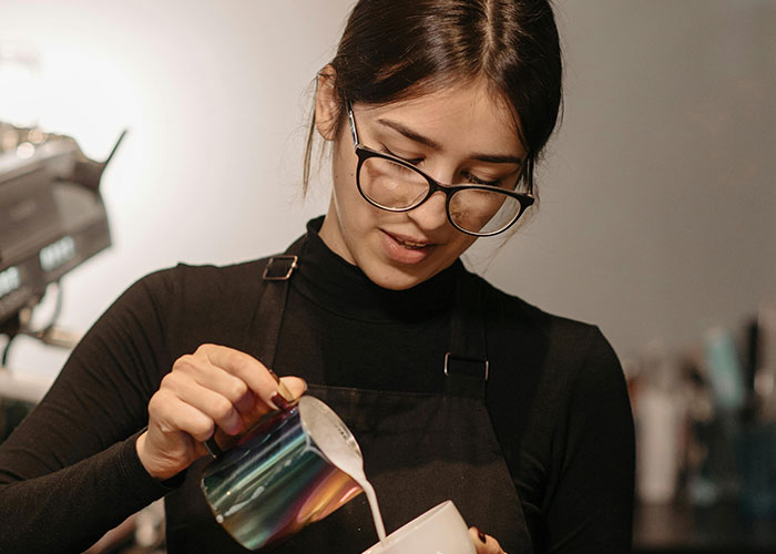 Young barista pouring milk into a cup at a coffee shop, illustrating economy and everyday work life.