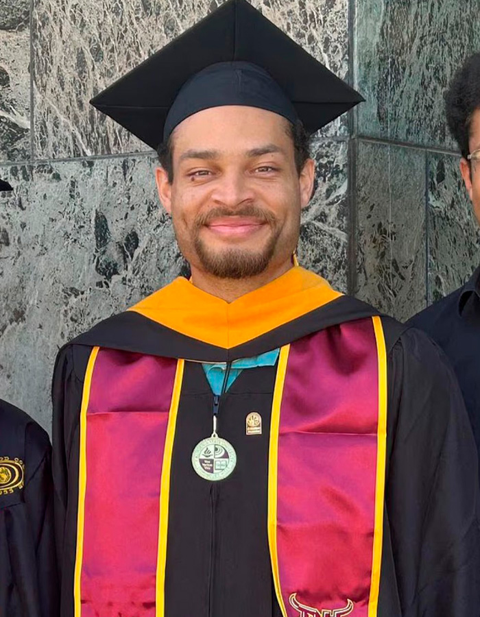 A smiling California teacher in a graduation cap and gown with burgundy and gold accents, symbolizing achievement.