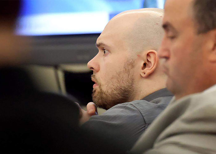 A bald, bearded FedEx driver in a gray shirt, looking left with an open mouth, likely in court.