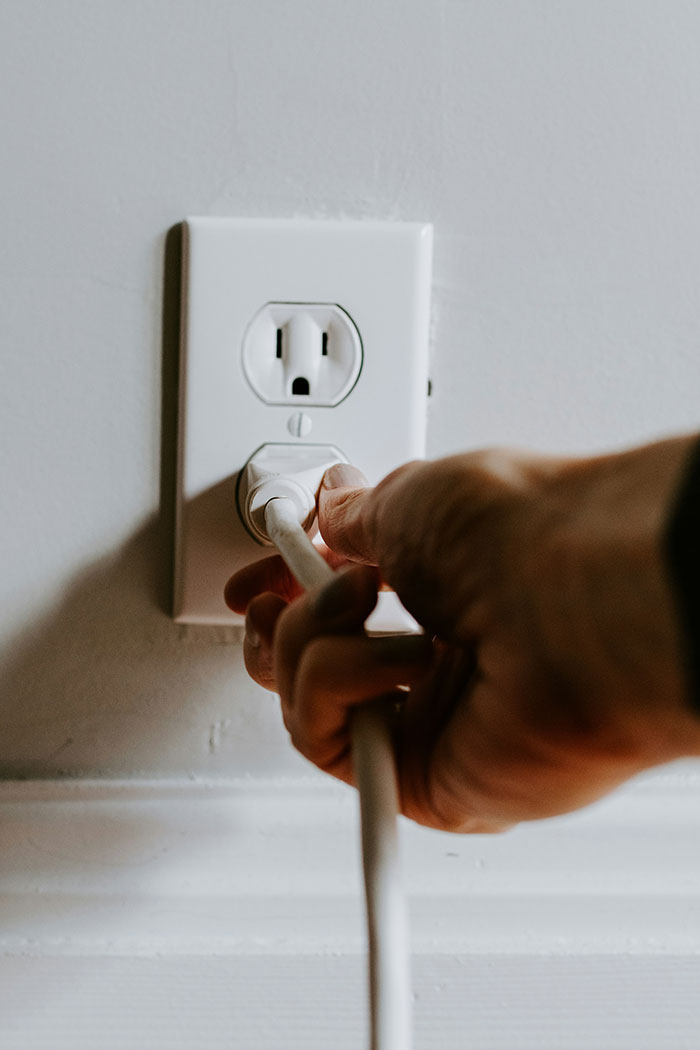 Hand plugging white electric cord into power outlet on white wall, symbolizing woman makes sister adopt her kid concept.