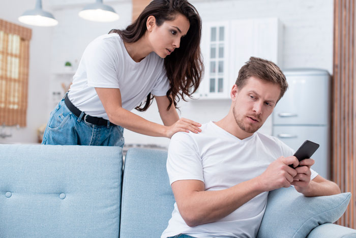 Uma mulher olha com desconfiança para o marido, que está absorto no telefone. Ela suspeita que ele tenha um filho secreto.