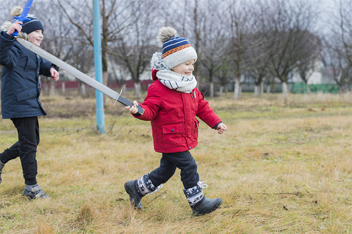 Two children playing outside with a toy sword on a grassy field during autumn, enjoying active playtime.